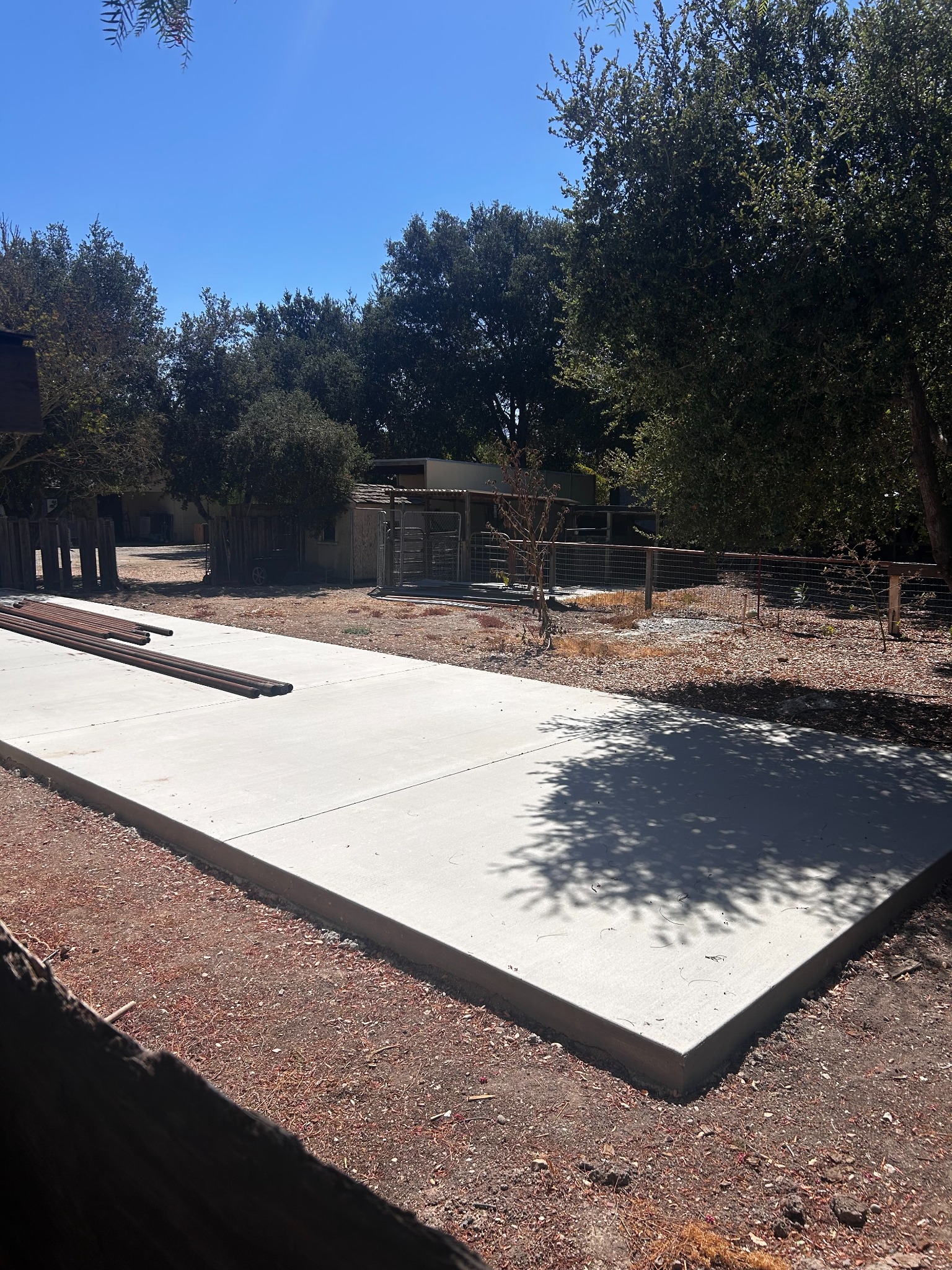 Concrete slab with construction joints, loose steel pipes, and outbuildings beyond